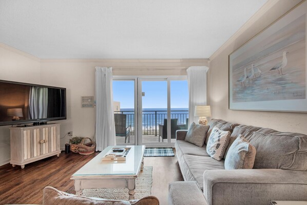 Uma sala de estar com televisão, sofá e vista para o mar.