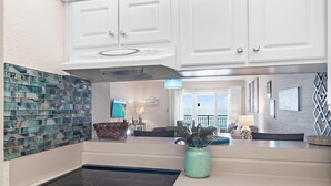 A modern kitchen with white cabinets, a black stovetop, and a backsplash with blue and green tiles. - Emerald Isle 708 (Fort Walton Beach)