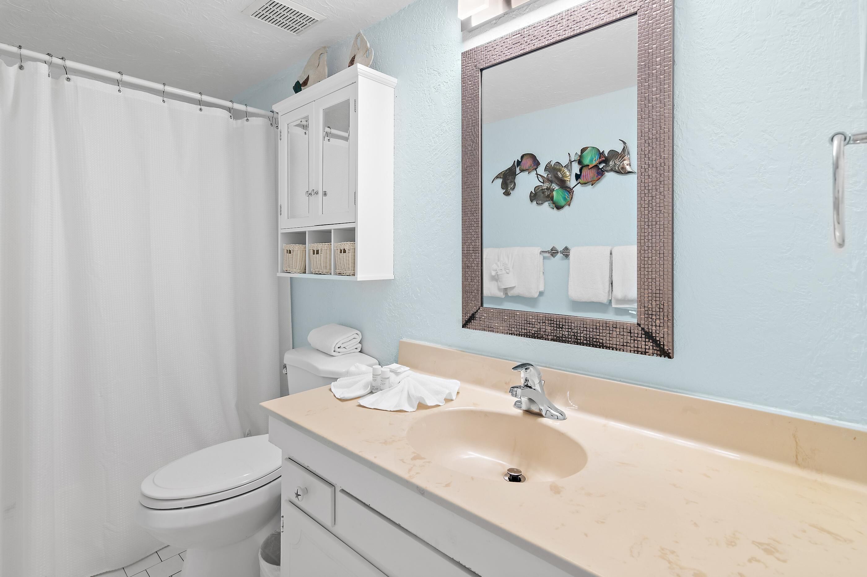 Een badkamer met een wit toilet, een beige wastafel en een spiegel met een decoratieve lijst.