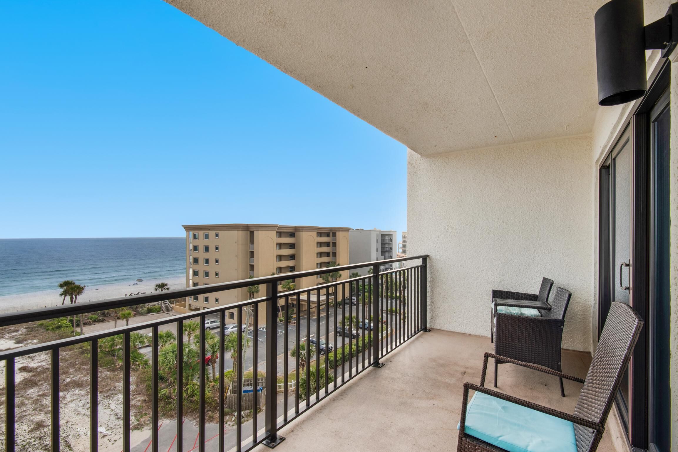 A balcony with a view of the beach and ocean, a chair, and a small table.