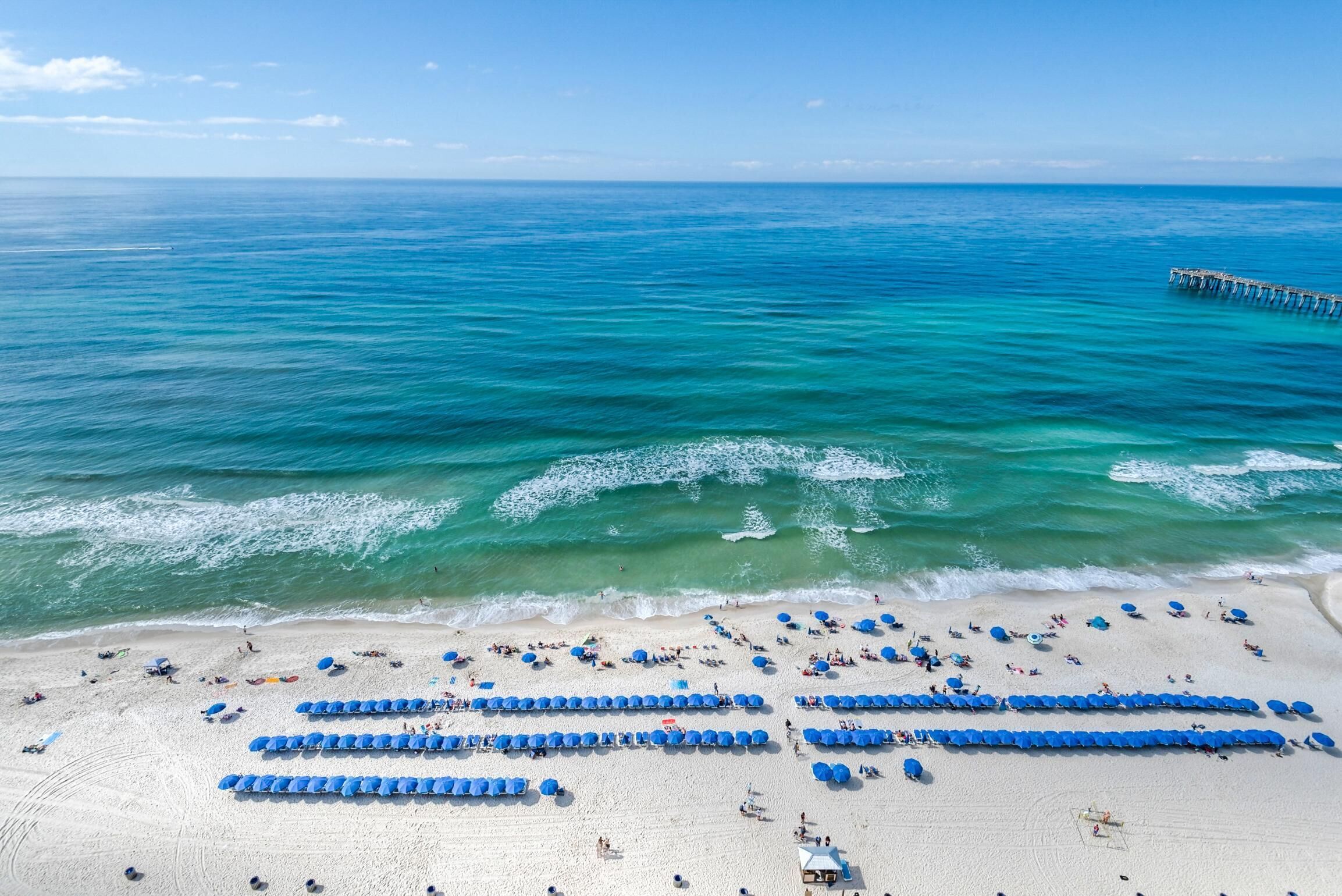 Una spiaggia con file di ombrelloni blu e bagnanti.