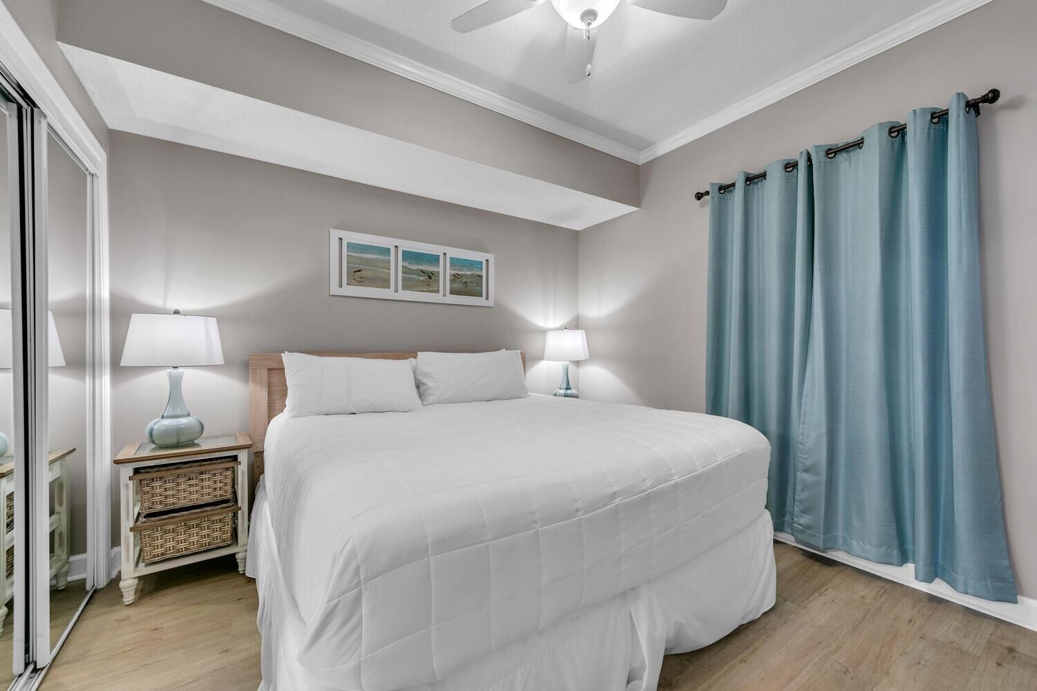 Une chambre avec un grand lit, deux tables de chevet avec des lampes, un ventilateur de plafond et une fenêtre avec des rideaux.