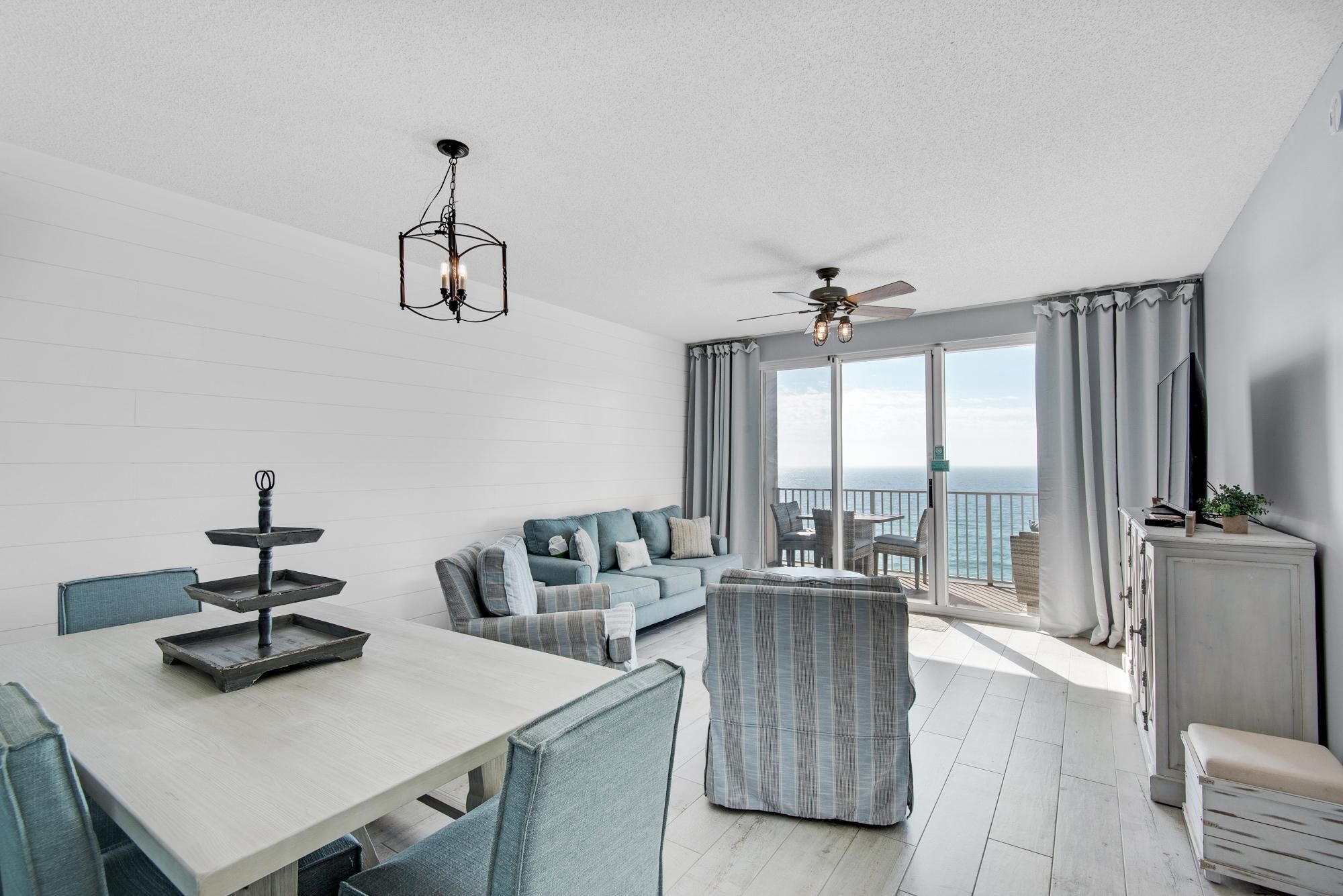 A modern living room with a dining area, a ceiling fan, and a view of the ocean.