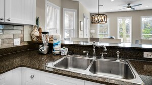 A kitchen with granite countertops, stainless steel sinks, and white cabinetry. There is a blender, a pitcher, and a jar on the counter. - A Piece of Heaven (Miramar Beach)