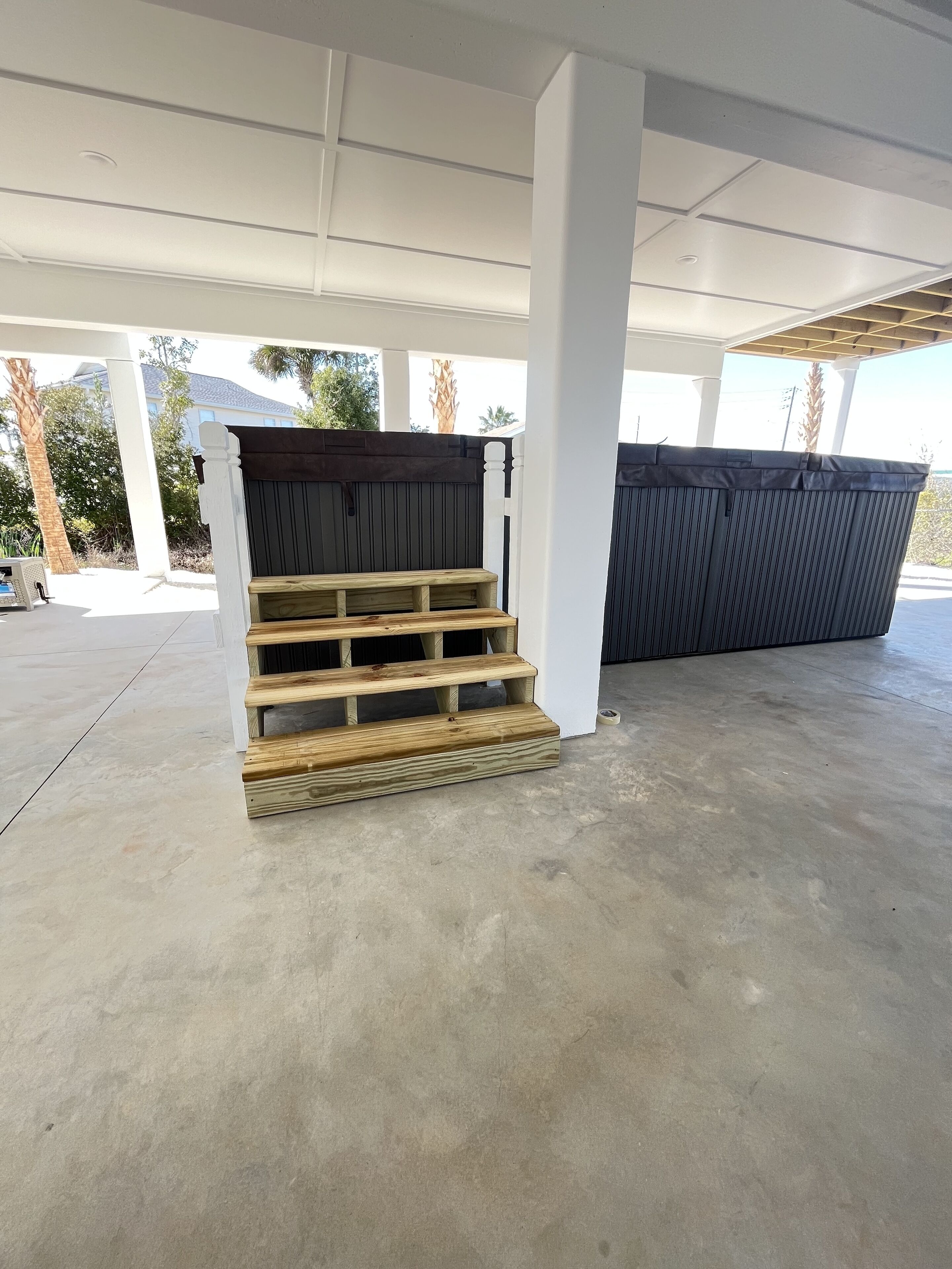 A covered outdoor area with concrete flooring, wooden steps, and a black fence.