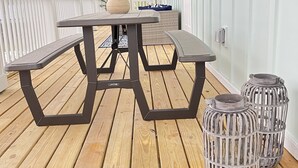 A wooden deck with a picnic table and benches, two lanterns, and a potted plant.