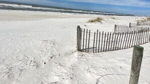 A sandy beach with a wooden fence and ocean waves in the background.