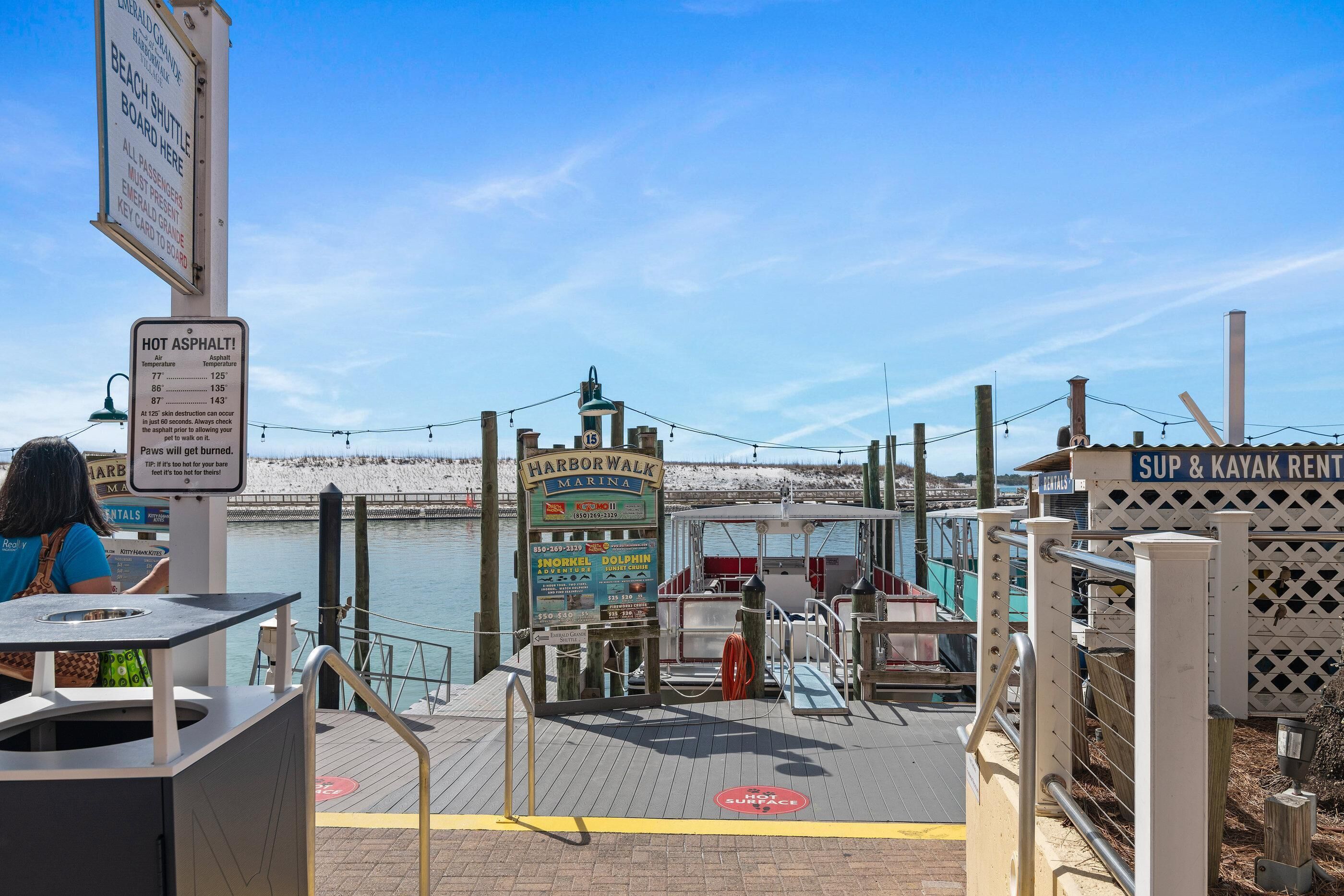 A waterfront marina with a dock, a sign for the Harbor Walk Marina, and a SUP & Kayak Rental sign.