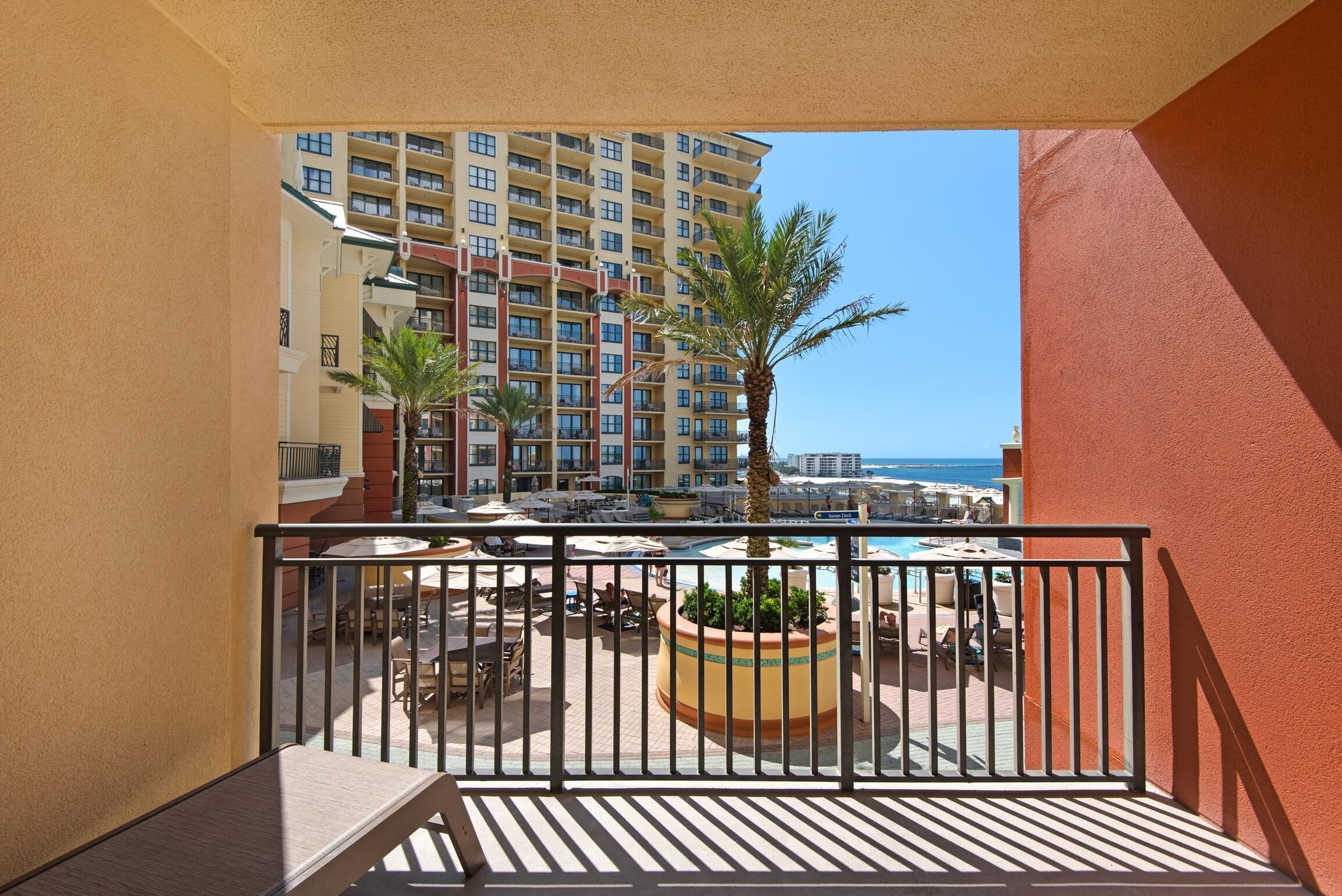 A balcony with a view of a pool area, palm trees, and a high-rise building in the background.
