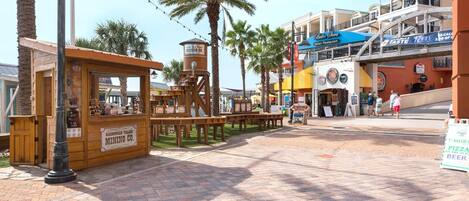 A street with a wooden mining exhibit, palm trees, and various shops including an Italian restaurant.