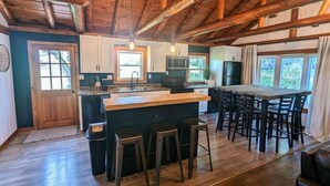 Een ruime keuken met een centraal eiland, houten balken en een eethoek met stoelen.