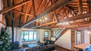 Een rustiek interieur met zichtbare houten balken, een open haard, een bank en een eettafel.