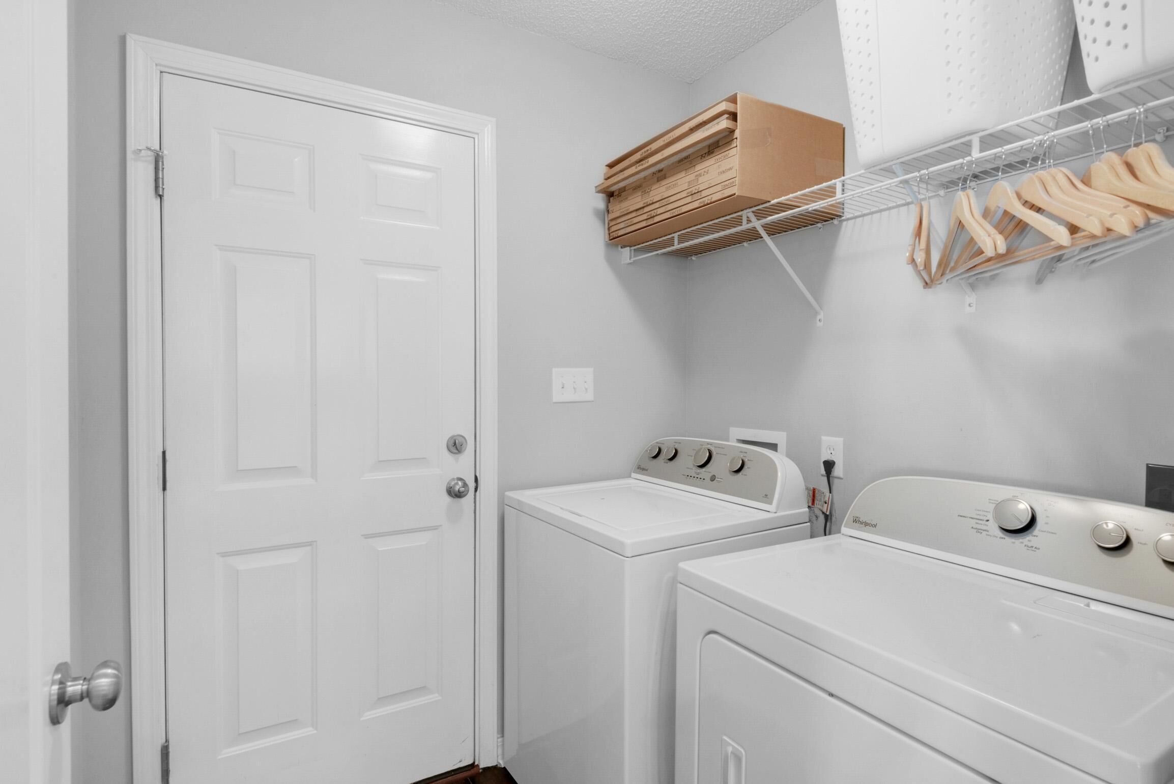 A laundry room with a white door, a stacked washer and dryer, and a metal rack with wooden hangers.