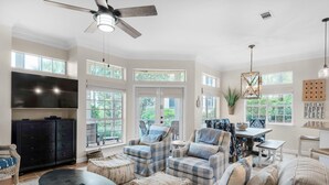 A spacious living room with a large TV, comfortable seating, and a ceiling fan.
