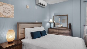 Ein Schlafzimmer mit Bett, Nachttisch, Nachttischlampe, Kommode, Spiegel und Klimaanlage.