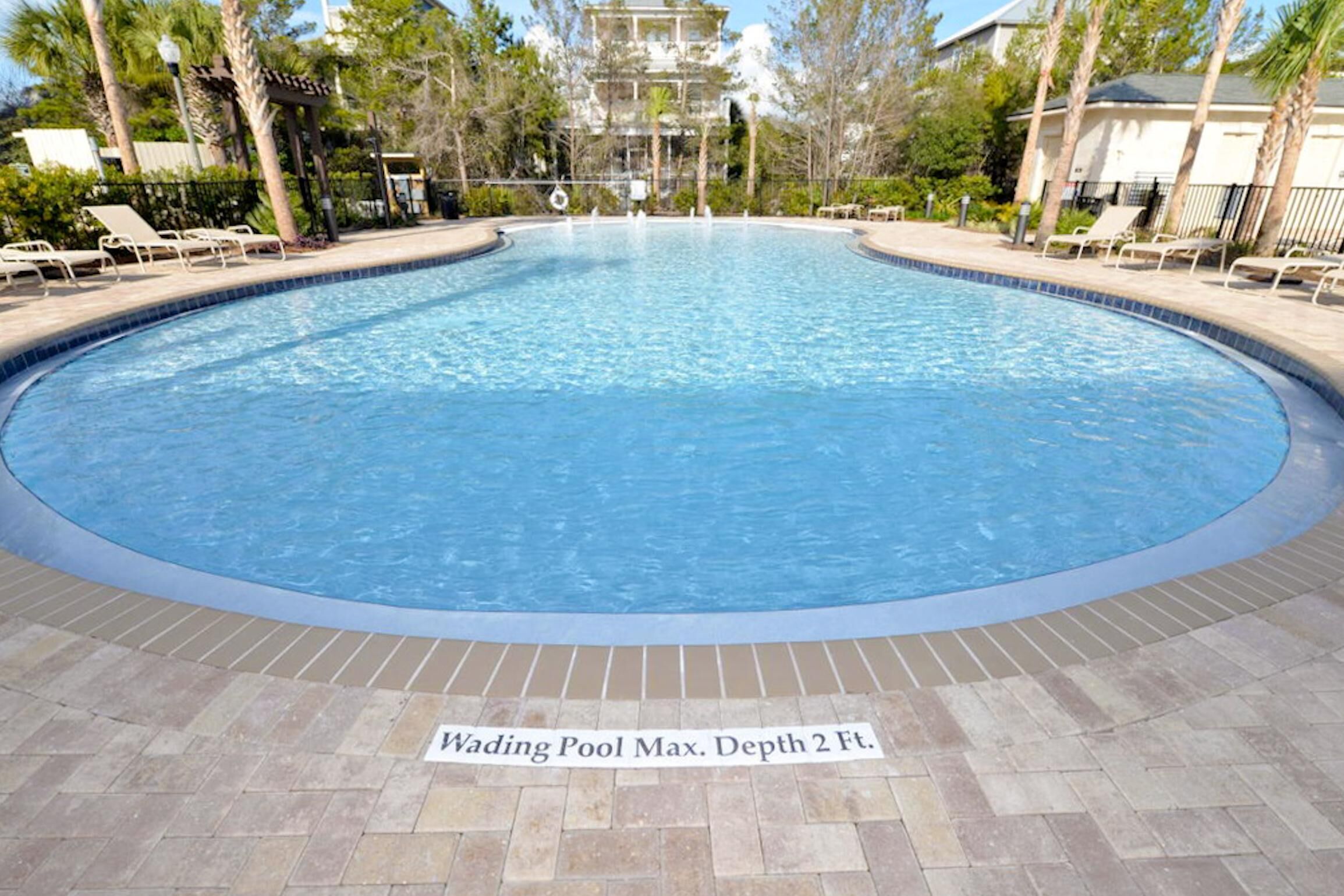 A circular wading pool with a maximum depth of 2 feet, surrounded by lounge chairs and palm trees.