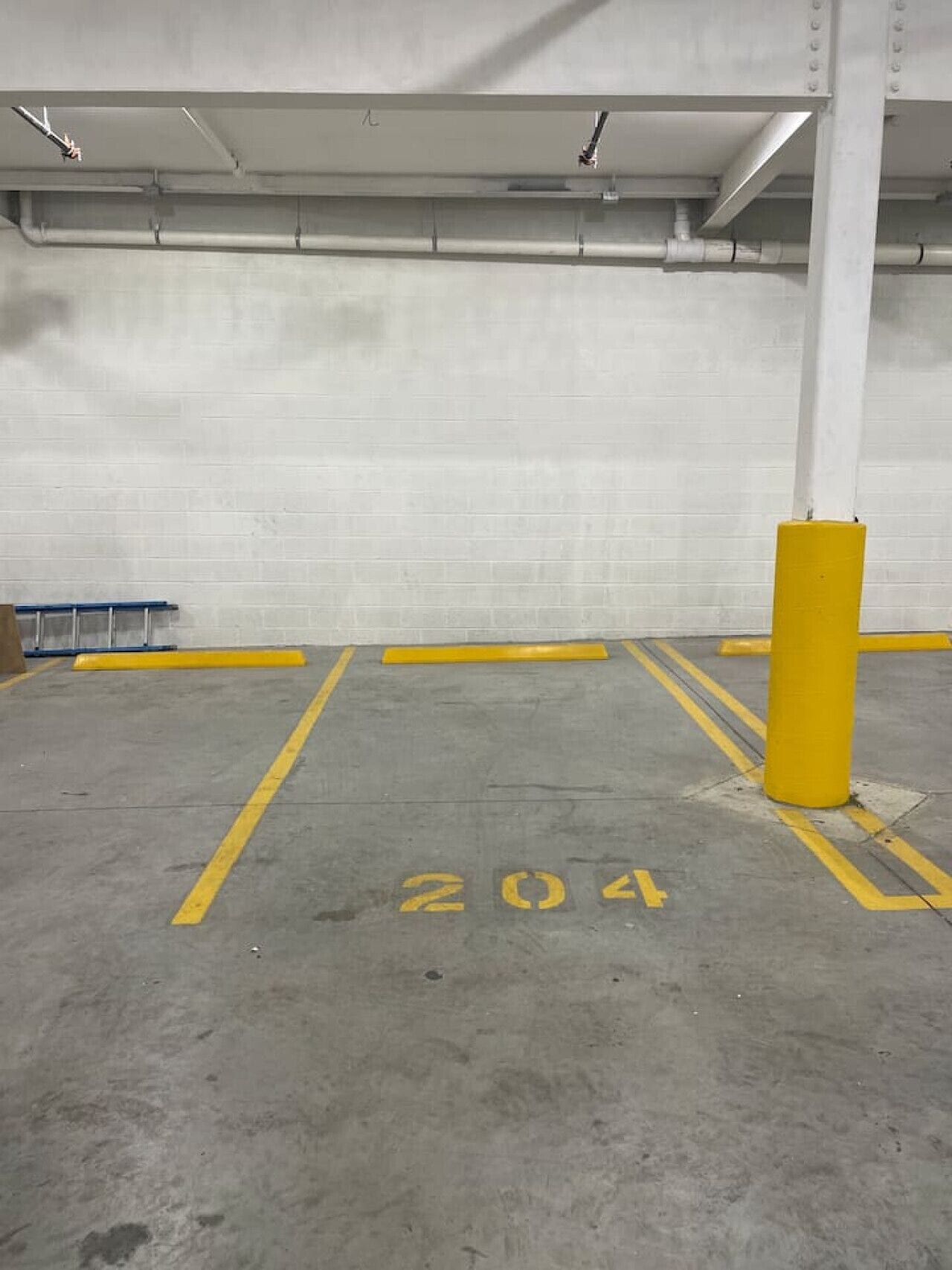 Un estacionamiento con paredes de concreto, un pilar amarillo y un espacio marcado con el número 204.