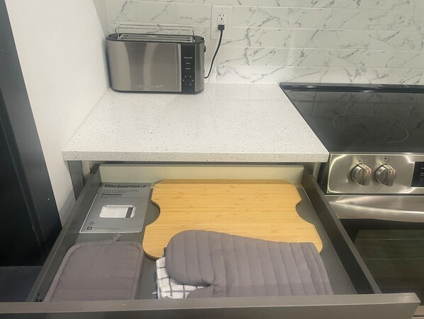 A kitchen with a toaster, a wooden cutting board, and a stainless steel stove.