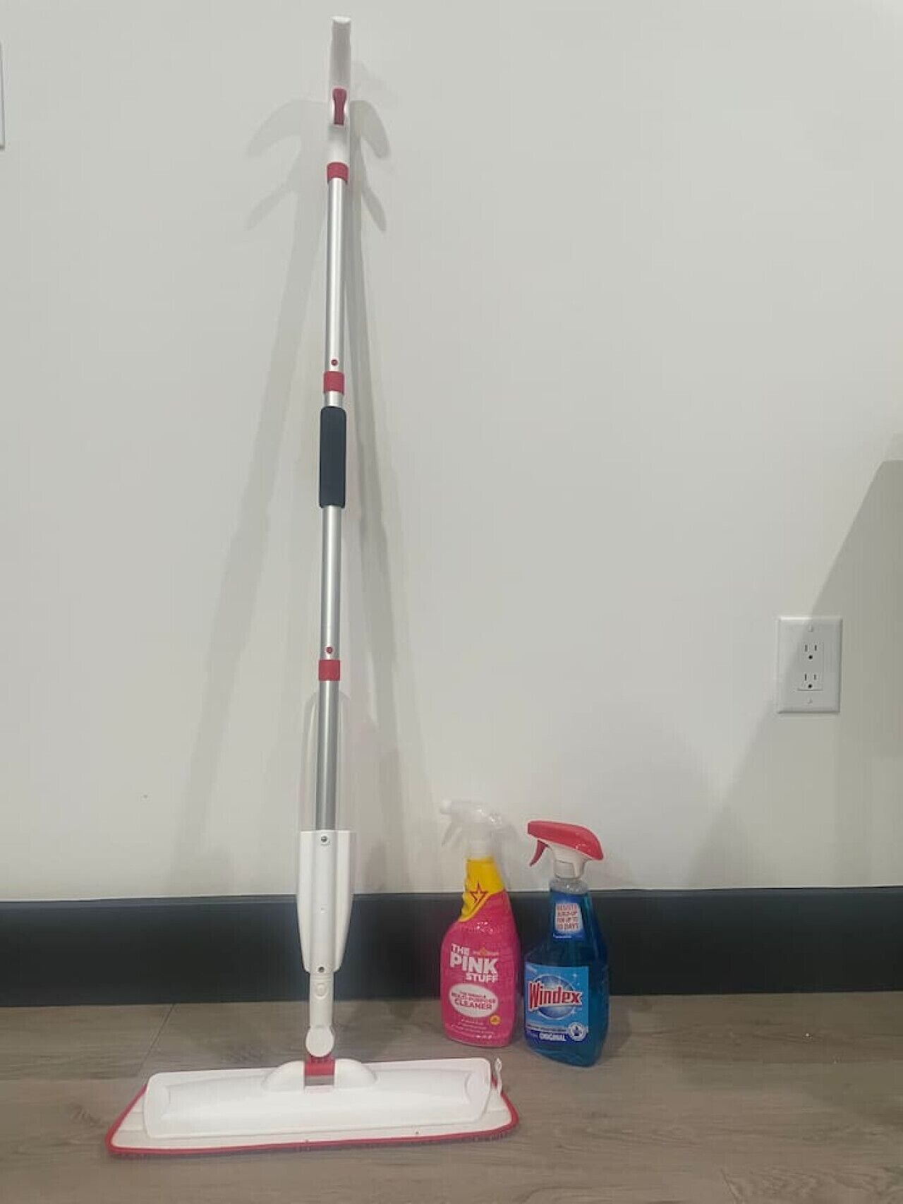 A mop, a pink cleaning product, and a blue cleaning product on a wooden floor.