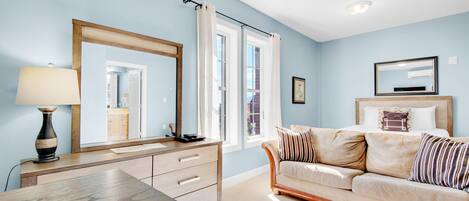 Una habitación con un escritorio de madera, un sofá color beige, un espejo grande y una ventana con cortinas.