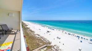 A balcony with a view of a beach, lounge chairs, and a clear blue sky. - Majestic Beach Towers 2-901 (Panama City Beach)