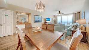 A spacious living area with a wooden dining table, a sofa, and a balcony with a view. - Majestic Beach Towers 2-901 (Panama City Beach)