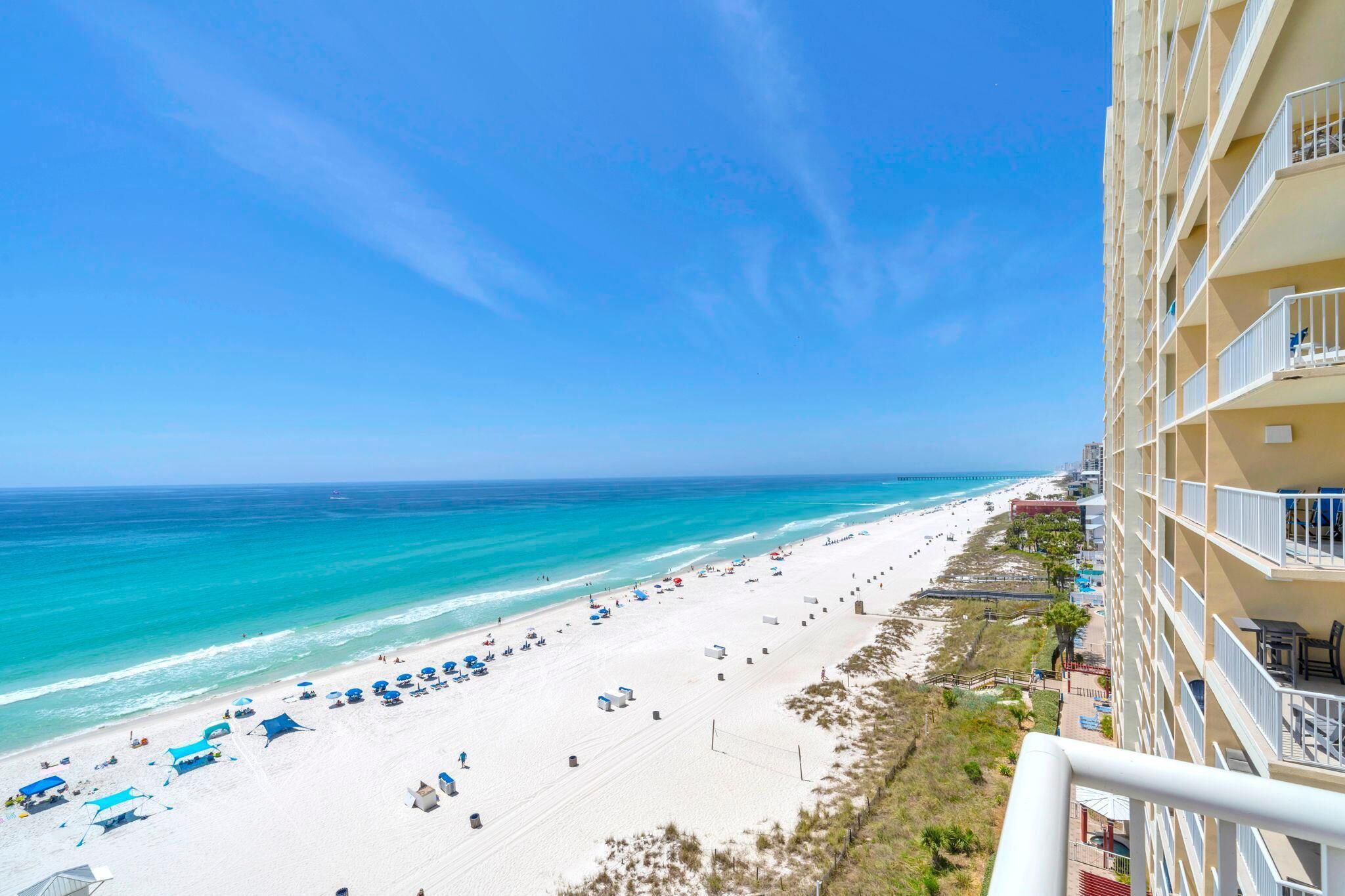 Vista de la playa desde un balcón de hotel, con cielo despejado, arena y el océano.