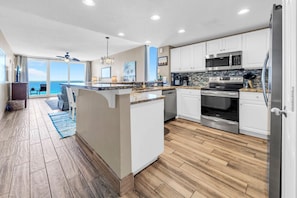 A modern kitchen with a central island, white cabinetry, stainless steel appliances, and a view to the outside. - Majestic Beach Towers 2-901 (Panama City Beach)