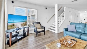 Ein modernes Wohnzimmer mit Flachbildfernseher, Deckenventilator, blauem Sofa und einer Treppe zu einer weiteren Ebene.
