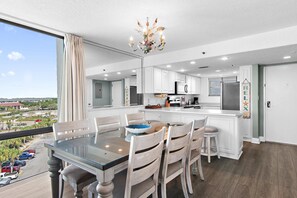 A modern kitchen with white cabinets, a central island, and a dining area with a glass table and wooden chairs. - Sundestin 818 (Destin)