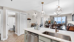 Une cuisine moderne dotée d’un grand îlot central, d’appareils électroménagers en acier inoxydable et de luminaires suspendus.