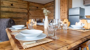 A wooden dining table set with white plates, bowls, and glasses, a vase with flowers, and a modern kitchen in the background.