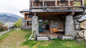 A stone building with a wooden deck, a wooden chair, and a view of mountains.