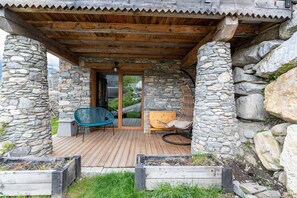 A stone building with a wooden deck, a wicker chair, a wooden bench, and a stone wall.