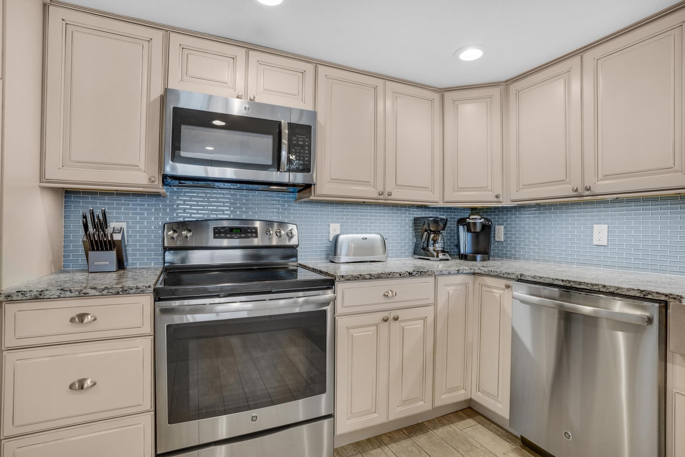 A modern kitchen with stainless steel appliances, light-colored cabinets, and a blue backsplash.