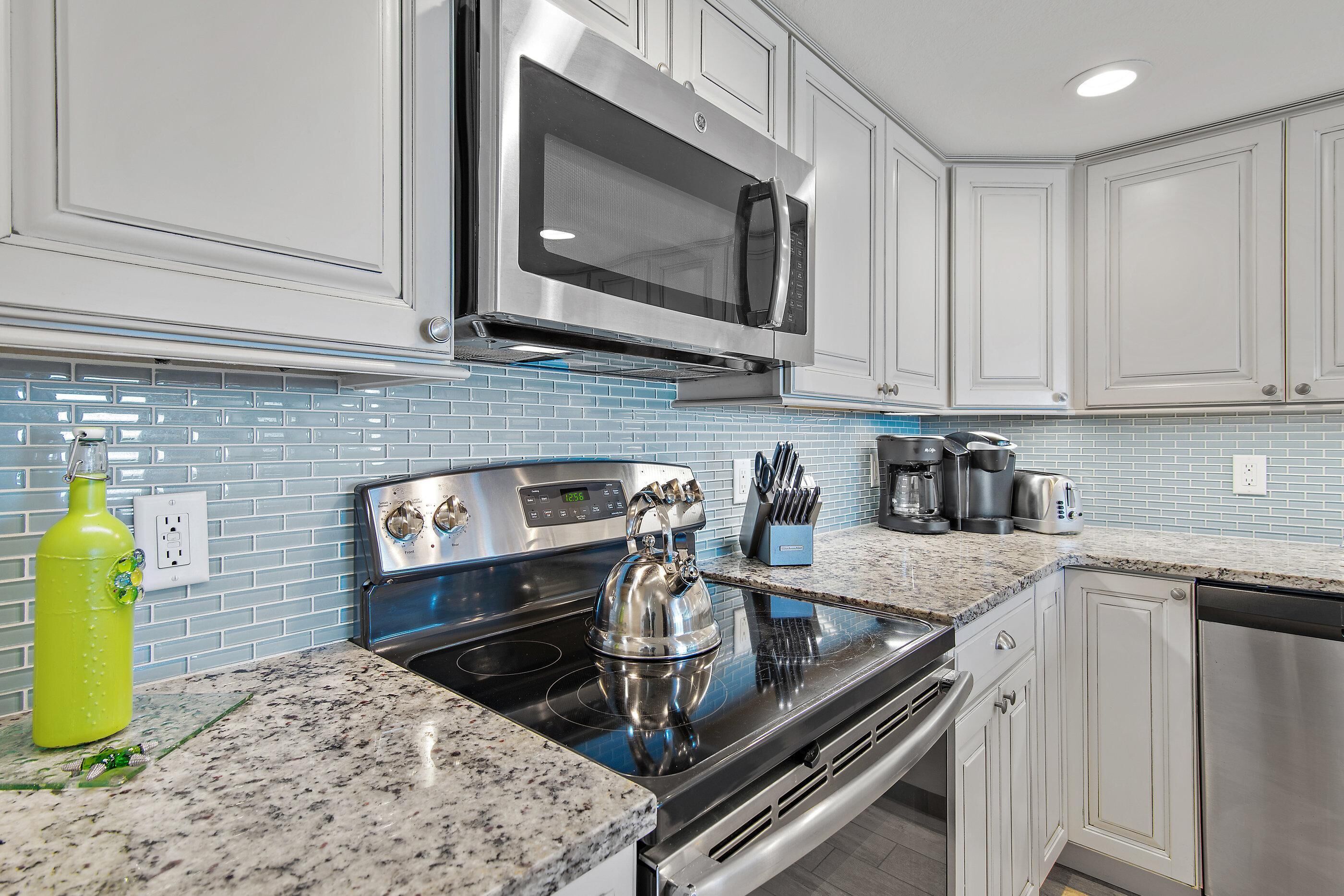A modern kitchen with stainless steel appliances, a microwave, and a kettle on the stove.