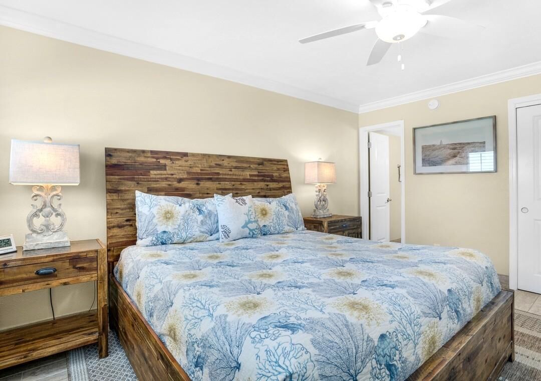 A bedroom with a wooden headboard, a floral bedspread, two bedside lamps, and a framed picture on the wall.