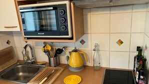 A kitchen with a Brandt microwave, a sink, a cutting board, a yellow kettle, a bottle of water, and a bottle of olive oil.