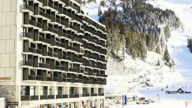 A multi-story hotel with balconies, located near a snowy mountain area.
