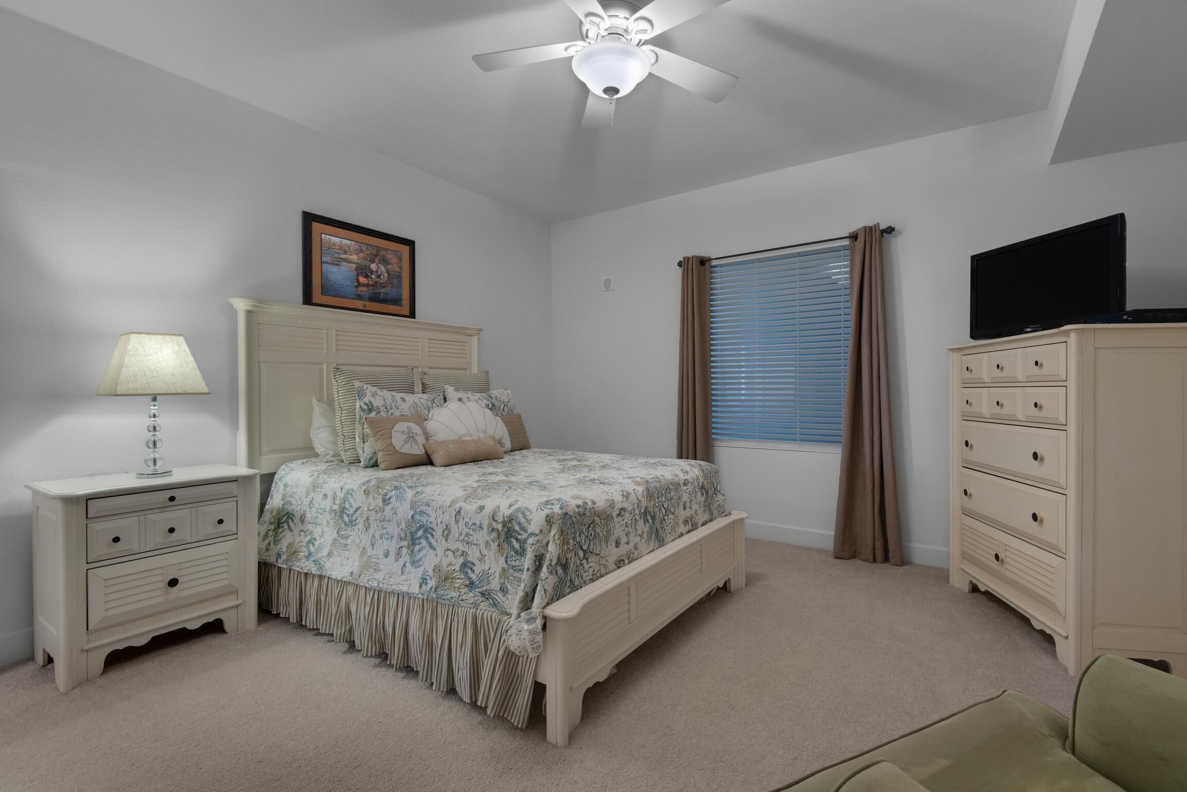 A bedroom with a bed, nightstands, a dresser, a ceiling fan, a window with curtains, and a television.