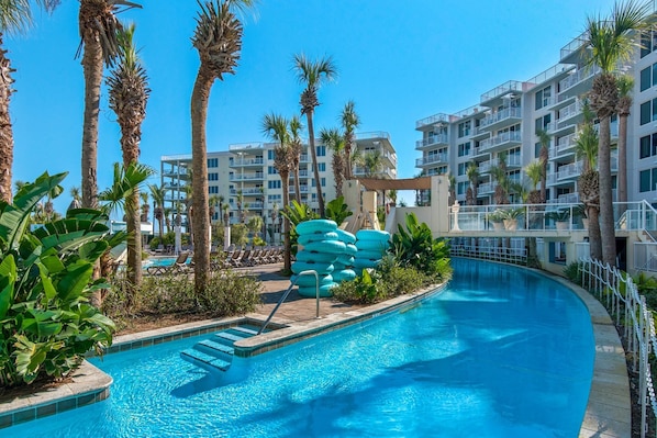 A swimming pool surrounded by palm trees and a multi-story building with balconies.