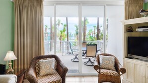 Ein Zimmer mit zwei Korbstühlen, einem Fernseher und einem Balkon mit Tisch und Stühlen.