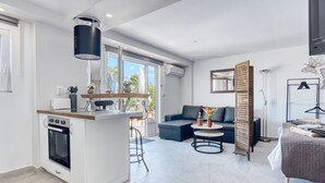 Une cuisine moderne équipée d’un four, un coin repas avec une table et des chaises, un canapé et un lit donnant sur l’extérieur.