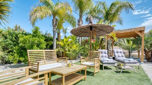 An outdoor seating area with wooden furniture, a thatched umbrella, and lush greenery. - Apartment 'Carpe Diem' with Shared Pool, Wi-Fi and Air Conditioning (Alicante (Alacant))