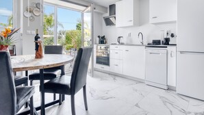 A modern kitchen with white cabinets, a dining table with chairs, and a view of greenery outside. - Apartment 'Carpe Diem' with Shared Pool, Wi-Fi and Air Conditioning (Alicante (Alacant))