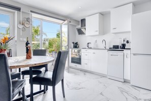 A modern kitchen with white cabinets, a dining table with chairs, and a view of greenery outside.