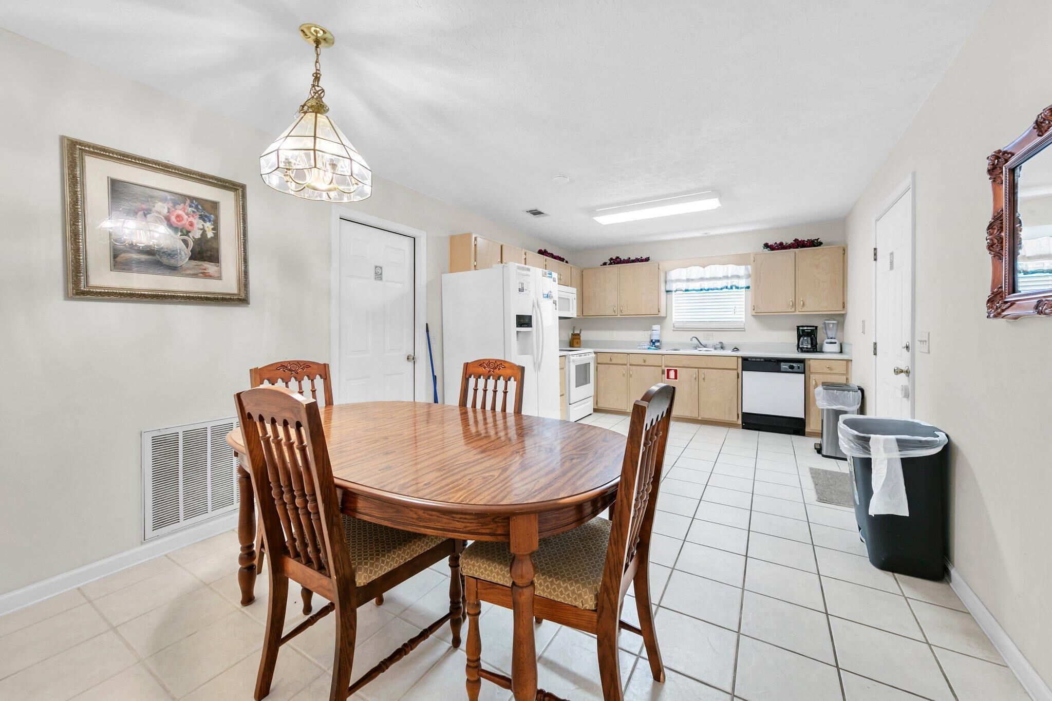 A dining area with a wooden table and chairs, a kitchen with white appliances, and a framed picture on the wall.