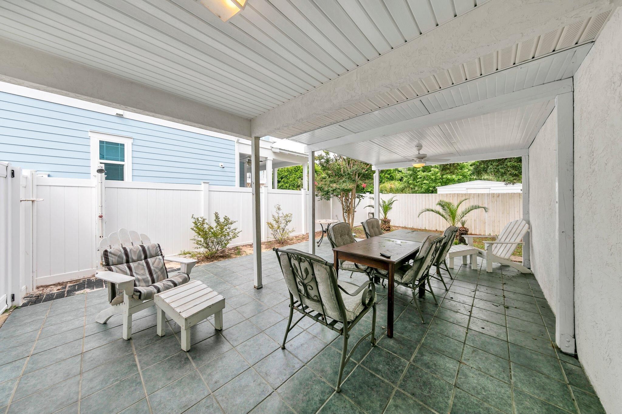 An outdoor patio with a table and chairs, a white fence, and a blue house in the background.