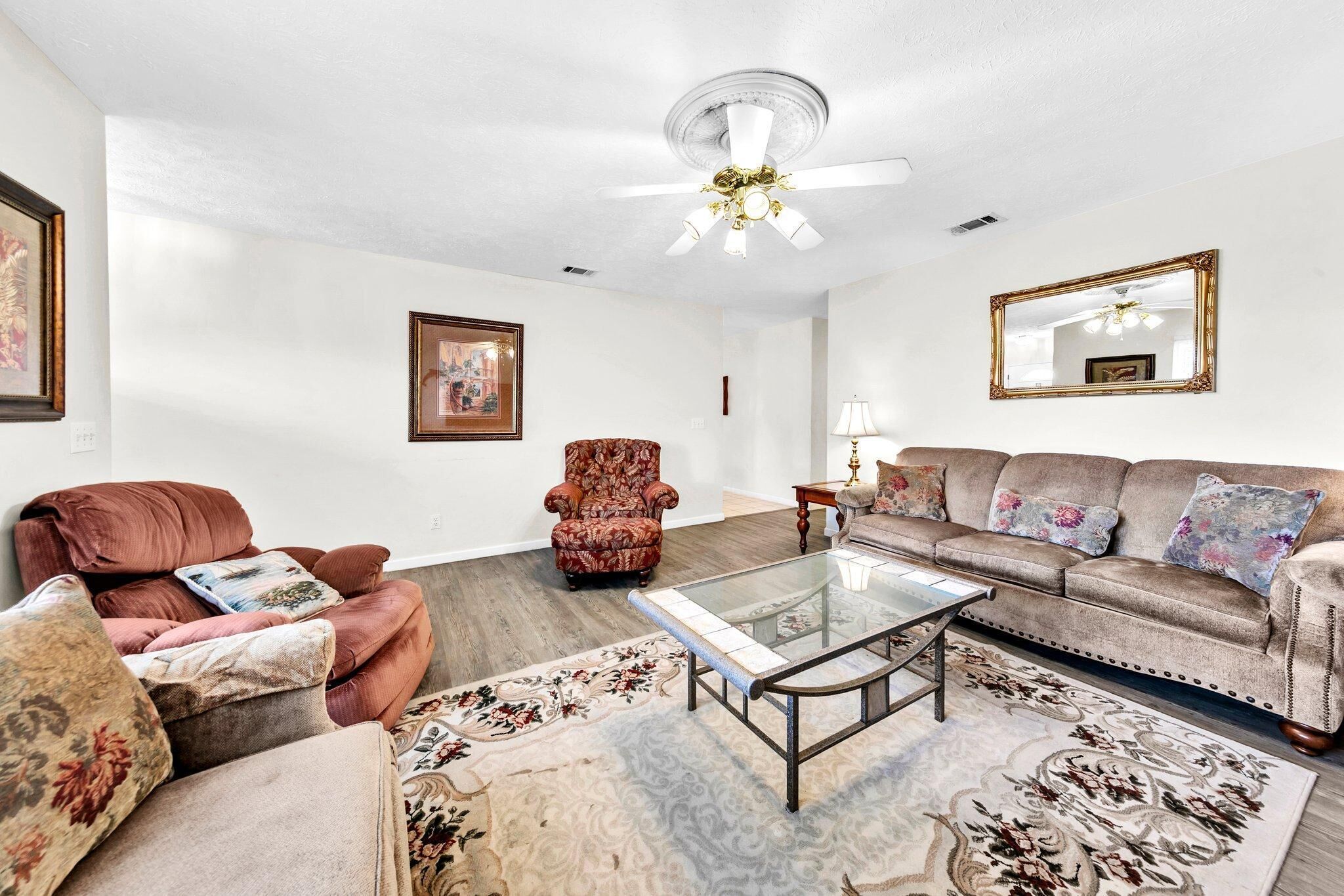 A living room with a brown sofa, a patterned armchair, a glass coffee table, and a floral rug.
