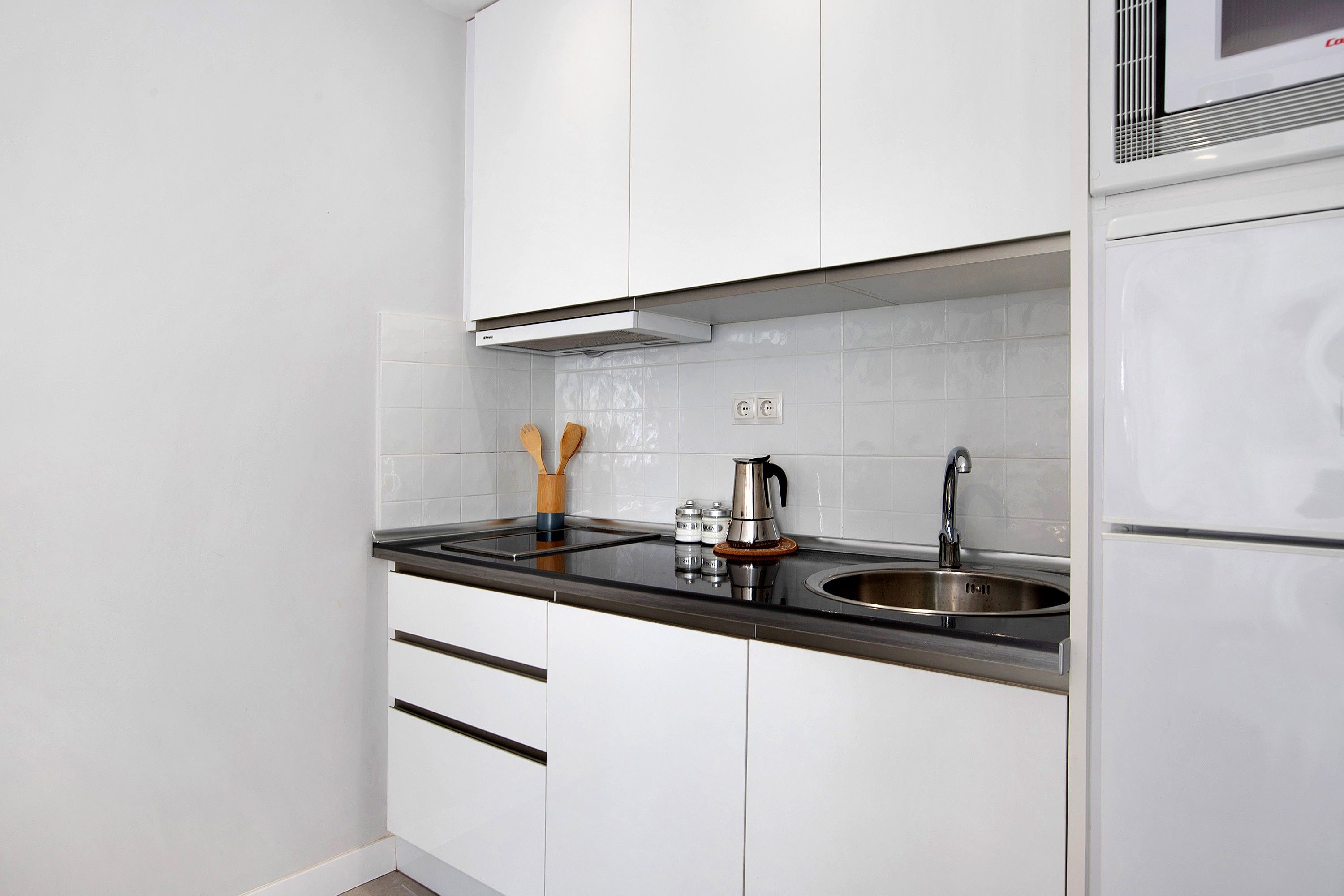 Una cocina moderna con armarios blancos, un lavamanos de acero inoxidable y una campana extractora integrada.